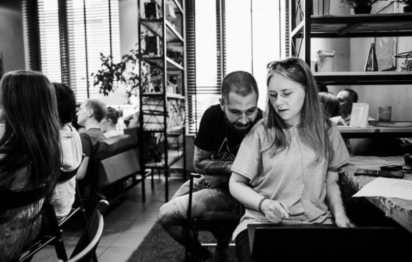 Work Shop Loft (Воркшоп Лофт). Зал 11 . Современное помещение с большими окнами, горизонтальными жалюзи и открытыми полками. На столе ноутбук и документы. Несколько человек сидят на стульях у деревянного стола. Комнатные растения и светлые стены. Чёрно-белое фото.