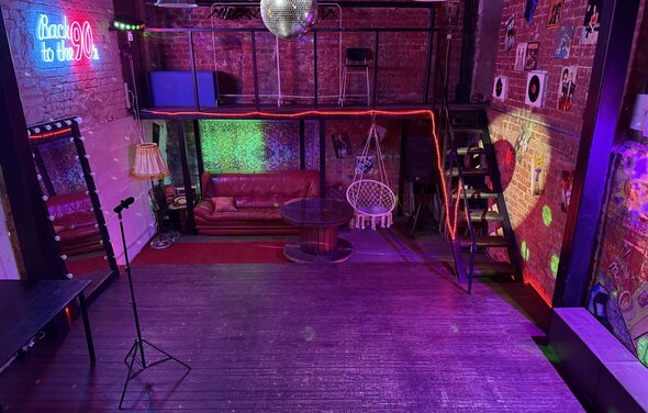 Лофт ИЗНАНКА. Зал ЛИХИЕ 90-е. Затемнённая комната лофта, много людей в кадре проводят фуршетное мероприятие, беря еду с объединённых столов. Несколько людей на кадре танцуют