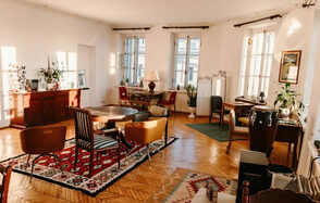 Светлый лофт с панорамным видом. Озарённое светом пространство. Столы со стульями. Ковры на полу. Различные элементы декора. Тумбочка