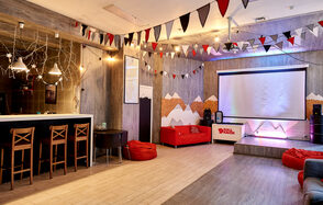 Стильный лофт в скандинавском стиле. Вход с улицы. Красный диван, сцена, большой экран, под потолком гирлянды из флажков.