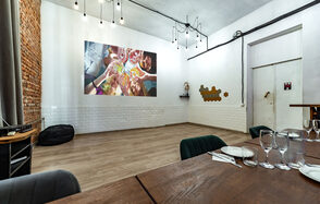 Rubin Loft (Рубин Лофт). Лофт средний. Просторная комната с кирпичной и белой плиточной стенами. В центре проекция на стене. Подвесные светильники на черных проводах. На переднем плане деревянный стол с сервировкой, стулья, бокалы, тарелки, приборы. Деревянный пол, пуфик.
