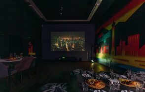 Зал Лас-вегас. Лофт-зал в американском стиле . Тёмная комната с проектором на стене, показывающим городской пейзаж. На стенах граффити со зданиями. Несколько столов с посудой и сервированными блюдами. Мягкие стулья серого цвета, тёмный деревянный пол. Слабое освещение.