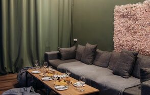 Зал Китай. Лофт-зал в китайском стиле . Просторная гостиная с серым угловым диваном и низким деревянным столом, сервированным бокалами и закусками. Зелёные шторы, стена с покрытием из розовых цветов. Деревянный пол. Мягкое освещение. Комната оформлена в спокойных тонах.