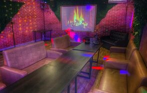 Forest(Лес). Уютное помещение с кирпичными стенами, темными деревянными столами и мягкими коричневыми диванами. На стене проекция камина. Пол из дерева. Разноцветное освещение создает атмосферу. В углу черный диван. На стенах зелень.