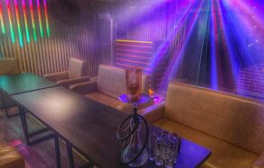 Forest(Лес). Тёмная комната с длинными столами, коричневыми диванами и креслами. На столе кальян и стаканы. Цветные световые эффекты и неоновая подсветка. Деревянные панели на стенах, кирпичная стена справа.