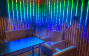 Forest(Лес). Угловое пространство с деревянными панелями на стенах, оборудовано мягкими диванами и прямоугольным столом. Вертикальные светодиодные полосы на стене создают разноцветное освещение. Цветовая палитра включает коричневый, синий, зелёный, и красный.