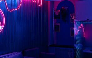 Rubin Loft (Рубин Лофт). Зал Токио. Современное пространство с металлическими стенами, украшенными неоновыми подсветками розового цвета. В углу — мягкие диваны. На стене картины, рядом панель с отверстиями и неоновыми линиями. Освещение приглушенное, синий фон.
