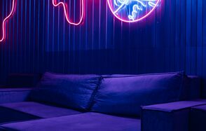 Rubin Loft (Рубин Лофт). Зал Токио. Лофт-пространство с темной мебелью, включая диван с подушками. Стена покрыта темными панелями, освещена неоновыми вывесками. Основные цвета — синий и сиреневый, создающие атмосферное освещение.