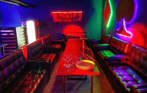 Rave(Рейв). Караоке-зал с длинным деревянным столом, окруженным кожаными диванами. На столе кальян и бокалы. Неоновые огни в виде мастей карт на стенах. Яркое разноцветное освещение, синий и красный интерьер. Декорировано постерами.