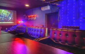 Rave(Рейв). Караоке-зал с диванами из коричневой кожи, темными деревянными столами и синим подсвеченным фоном. На стене проектор и гирлянда из огней. Настенное кондиционирование, неоновая вывеска, декорации в виде карт.