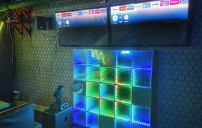 Bee-lounge(Пчела-лаундж). Караоке-зал с двумя настенными экранами, светодиодная панель с разноцветной подсветкой. Обои с геометрическим узором, потолочные коммуникации, колонки. Мягкие стулья, приглушенное освещение.