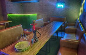 Bee-lounge(Пчела-лаундж). Караоке-зал с кожаными диванами вдоль стен, длинным деревянным столом и барной стойкой с зеленой подсветкой. На столе стеклянные бокалы, тарелки и кальян. Стены с узором, неоновая вывеска на стене.
