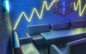 Bee-lounge(Пчела-лаундж). Кожаные диваны и прямоугольный стол в углу помещения. Синие стены с шестигранным узором. Светодиодные желтые неоновые линии на стене. Полумрак, освещение неоновое. Состояние мебели и отделки хорошее.