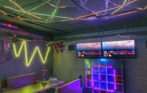 Bee-lounge(Пчела-лаундж). Караоке-зал с неоновыми огнями, светодиодными лентами на потолке, мягкими диванами и деревянными столами. На стене два телевизора, светящаяся панель и декоративные элементы. Стены декорированы узорчатой плиткой. На столе кальян и бутылки с водой.