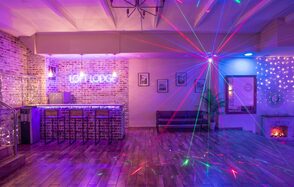 Loft Lodge (Лофт Лодж) 7. Просторный уютный лофт. Лофт-пространство с кирпичными стенами и деревянным полом, барная стойка с табуретами, неоновая надпись, световые эффекты, потолочные балки, декоративный камин, художественные рамки на стене, мягкая мебель, гирлянды из лампочек.