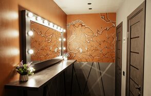 Nord Loft(Норд Лофт). Гримерная комната с большим зеркалом, обрамленным лампочками. На стене изображена карта. Стены и двери темного цвета. На длинной столешнице стоит вазон с цветами. Потолок светлый с несколькими встроенными светильниками.