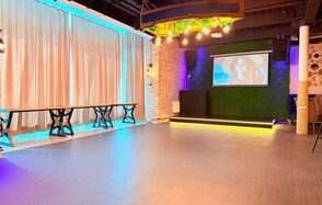 Лофт Фантом. Просторное помещение с деревянным паркетом и светодиодным освещением. Белые кирпичные стены, большие светлые шторы, деревянные столы. На одной стене экран с проектором, оформленная зелёной растительностью. Потолок декорирован светодиодными лампами.