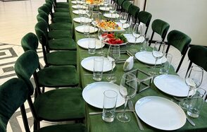 Arcobaleno Loft(Аркобалено Лофт). Длинный банкетный стол с зеленой скатертью и рядами темно-зеленых стульев, сервирован белыми тарелками, бокалами и приборами. На середине стола блюда с закусками. Пол с узором светлых и темных плиток.