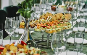 Arcobaleno Loft(Аркобалено Лофт). Длинный банкетный стол с зелёной скатертью, сервирован тарелками с разнообразными канапе, бокалами для вина и стеклянными стаканами. Вазы с цветами украшают стол. Цвета: зелёный, белый, металлические элементы.