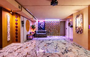 Стильный лофт Джаванди. Пространство с мраморным полом, светлыми стенами и подвесным потолком. Элементы декора: постеры, круглые панели, неоновая вывеска. Мебель: диван, столик, кресло. Освещение: встроенные светильники, неон. Стены украшены растениями.