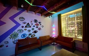 Яркий двухуровневый лофт. Приглушённый свет. Диваны. Стена с рисунками. Окно со светящейся гирляндой