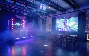 Лофт с верандой, мангалом и сценическим оборудованием. Праздничное пространство в стиле лофт с деревяными балками на потолке и паркетным полом. DJ-стойка с неоновыми огнями и надписью. Зал с деревянными столами и стульями. Дискобол и проекция на стене. Мягкое разноцветное освещение.