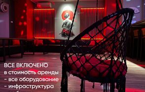 Лофт ИЗНАНКА. Зал ТОКИО. Пространство с подвесным креслом, креслом-мешком, столами вдоль стены, которое украшает картина. Настенный декор с подсветкой. Красные неоновые элементы освещения. Текст: «Все включено в стоимость аренды - все оборудование - инфраструктура».
