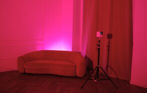 Стильный лофт для уютных вечеринок. Розовая подсветка, диван полукруглой формы, паркетный пол, шторы, стена с декоративными панелями, штатив с проектором, минималистичный интерьер, текстурированные материалы, отсутствие текстов и знаков.