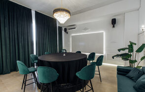 Rubin Loft (Рубин Лофт). Зал Империал. Круглый стол с черной скатертью окружен зелеными стульями. Потолочный светильник в виде люстры. Зеленые шторы от пола до потолка. Белые стены, одна с подсветкой. В углу комнатное растение. Бежевый пол. По бокам настенные динамики.