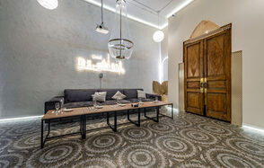 Rubin Loft (Рубин Лофт). Зал Дубай. Большая комната с серым диваном вдоль стены, перед которым стоит длинный деревянный стол с черными металлическими ножками. Подвесные светильники и неоновая надпись на стене. Декорированные деревянные двери и орнаментальная плитка на полу.