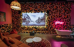 Лофт Гламур. Лофт с леопардовым принтом на стенах, диван, круглый ковёр, два круглых столика, ванна, неоновая надпись "Glamour", большой экран, лампа с абажуром, красные и розовые тона, комбинированное освещение.