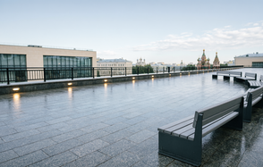Площадка в Москве. Открытая терраса с серыми плитами, ограждение из металла с подсветкой, скамейки из дерева с серыми металлическими основаниями. На фоне видны здания с куполами. Небо ясное с облаками.