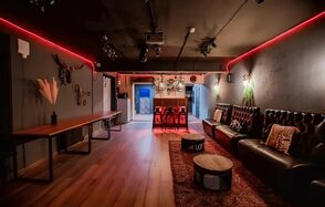 Пространство для любых мероприятий с верандой и грилем. Лофт-пространство с деревянным полом, черной и красной цветовой гаммой. Мебель: длинный деревянный стол, коричневый кожаный диван, круглые столики. Освещение: красные неоновые лампы, настенные светильники. Декор: растения, картины, декоративные головы животных.