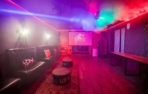 Пространство для любых мероприятий с верандой и грилем. Караоке-зал с приглушенным освещением, диванами черного цвета вдоль стены, пуфами, большим экраном для проектора. Деревянный пол, ковровое покрытие, стол вдоль правой стены. Светодиодные ленты на потолке, декоративные элементы на стенах.