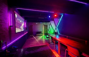 Kahovka loft (Каховка Лофт). Неоновый лофт-зал. Караоке-комната с длинным деревянным столом, стульями, экраном на стене. Стены и потолок украшены светодиодными лентами фиолетового и зеленого цветов. На полу плитка и паркет. Яркое разноцветное освещение.