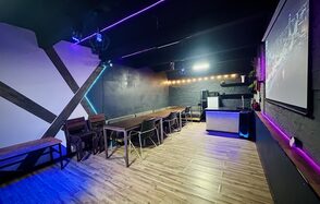 Kahovka loft (Каховка Лофт). Неоновый лофт-зал. Современное пространство с деревянным полом, стены отделаны черными и белыми панелями, потолок черный. Ряды стульев и столов, барная стойка, большой экран. Светодиодная и неоновая подсветка, гирлянды.