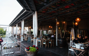 Soho Country Club (Сохо Кантри Клаб). Открытая терраса с деревянным полом и крышей, выбеленными колоннами, множеством деревянных столов и стульев. Подвесные светильники, горшок с растениями и обогреватели. На столах белая посуда. В кадре несколько людей за столами.