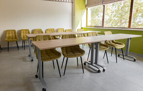 Зал 5. Светлый малый конференц-зал до 20 человек в Академии Кантаты. Конференц-зал с бежевыми стульями и столами на колесиках. Светлая комната с большими окнами, светло-зеленые и белые стены, серый пол. Естественное освещение из окна. Жалюзи частично опущены.