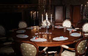 Polygon(Полигон). Зал Апартаменты. Круглый деревянный стол с расставленными вокруг стульями, на столе карточные наборы и стаканы. Центральная композиция из свечей на подсвечниках. Низкое освещение, стены из кирпича.