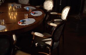 Polygon(Полигон). Зал Апартаменты. Круглый деревянный стол с набором кружевных подставок, на них стаканы и разноцветные плотные кружки. Вокруг стола стоят классические стулья с подлокотниками и светлой обивкой. Освещение теплое, направлено сверху. Пол тёмный.