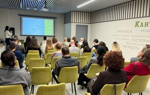 Зал 6. Просторный и светлый конференц-зал до 50 человек в Академии Кантаты. Зал с проектором и экраном, перед которым сидят люди на светло-зеленых стульях. Серые стены с деревянными элементами, на одной из стен текст с крупными словами. Потолок с ламелями, встроенное освещение.