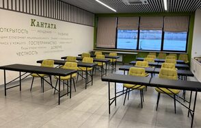 Зал 6. Просторный и светлый конференц-зал до 50 человек в Академии Кантаты. Учебное помещение с черными столами и желтыми стульями, расположенными в рядах. Окно с жалюзи, светлые плиточные полы, зеленая стена с текстом. Потолок с линейными светильниками. Состояние хорошее, естественное и искусственное освещение.