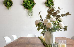 White Loft(Белый лофт). Уютный светлый лофт . Столовая с деревянным столом, вокруг белые стулья. На столе большие белые цветы в керамической вазе и несколько свечей. Белые стены украшены круглыми кашпо с зелеными растениями. Естественное освещение.