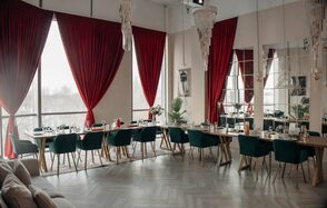 Зал Олд Мани. Лофт в индустриальном стиле. Просторное помещение с большими окнами и красными шторами. Длинные деревянные столы с сервировкой и зелёными стульями. Потолочные люстры. Светлые стены и паркетный пол. Зеркала на стене. Справа видна часть дивана.