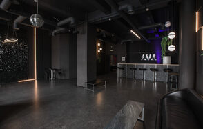 Rubin Loft (Рубин Лофт). Лофт Блэк. Темное индустриальное пространство с бетонным полом и черными стенами. Высокие потолки с видимыми коммуникациями. Барная стойка с высокими черными стульями. Слева подвесная диско-шар. Мягкая зона с диваном. Неоновая надпись на стене.