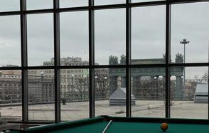 Студия Н. Современное остеклённое пространство с видом на город, большое окно от пола до потолка. В комнате бильярдный стол с зелёным сукном и шаром. Снаружи видно террасу с фонарями и фрагменты городской архитектуры.