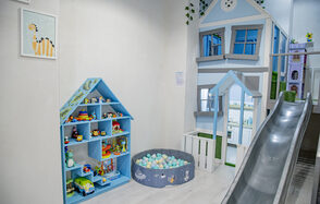 Лофт Облака. Зал Баунти на Полярной. Детская игровая зона с горкой, стеной в виде дома и игрушечным домиком. Голубой стеллаж с игрушками и круглым бассейном с мягкими шарами. Светлые стены, частичное зелёное растение на стене, картина с тигром.
