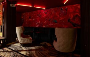 Микс Afterparty(После вечеринки). Лаунж-зона с двумя высокими белыми стульями, черным диваном, столиком. Красные абстрактные рисунки на стене. Потолочные красные светильники, ковровое покрытие с узором. Текстуры дерева на колоннах и полу.