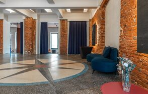 Quattro Space. Зал Компас. Лофт-пространство с кирпичными стенами, пол с узором компас, сине-зеленый диван, черные и темно-синие занавески, розовый стол с вазой и сухоцветами. Белый потолок с встроенным освещением, большие окна.
