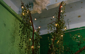 Хендмейдщики. Лофт в лесной тематике. Зеленая комната с декоративными ветвями, обвитыми гирляндой мелких лампочек. Стены и потолок окрашены в зеленые и голубые оттенки с рисунками звезд. Плотная растительность украшает интерьер, добавляя естественные элементы.